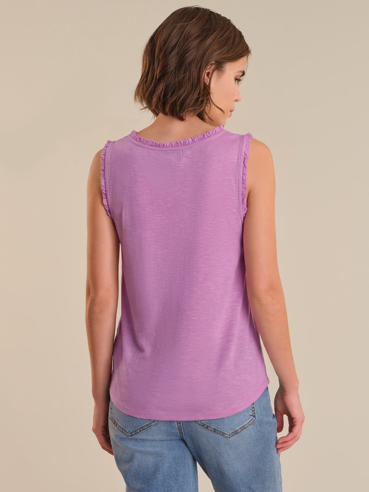 Woman wearing a purple sleeveless top and blue jeans on a beige background