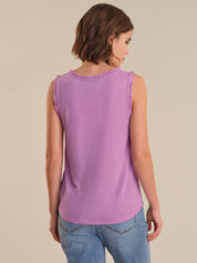 Woman wearing a purple sleeveless top and blue jeans on a beige background