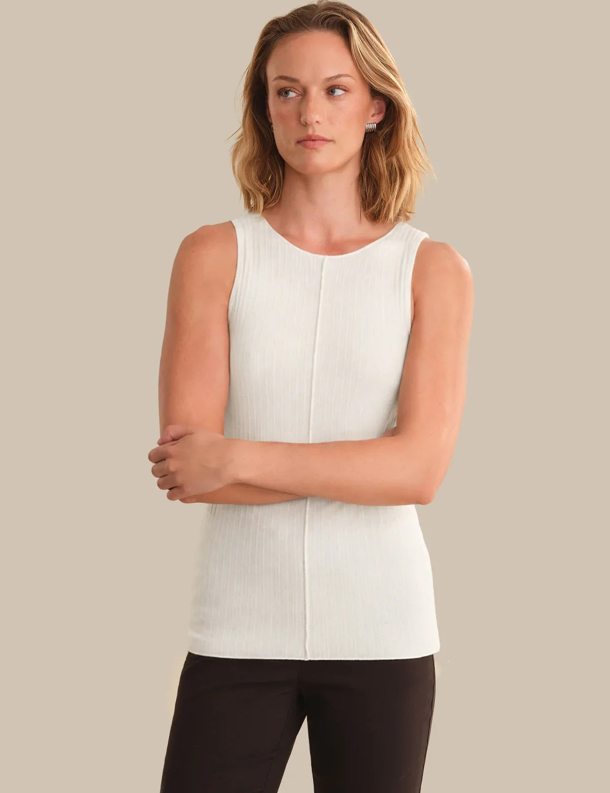 Woman wearing a white sleeveless top against a beige background