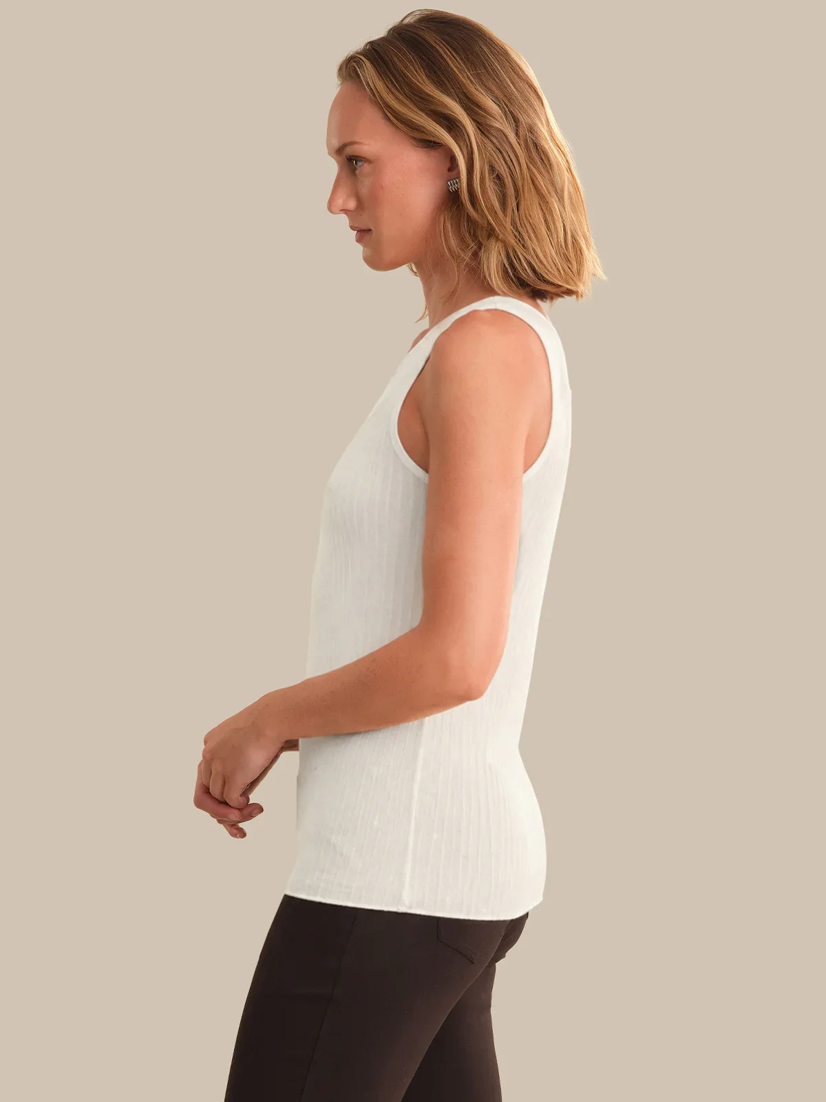 Woman wearing a white sleeveless top against a beige background