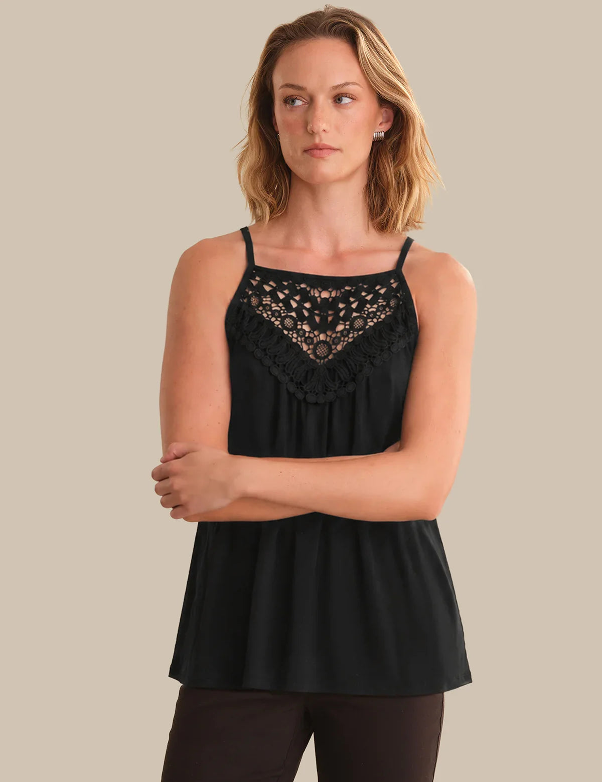 Woman wearing a black sleeveless top with lace details on a beige background