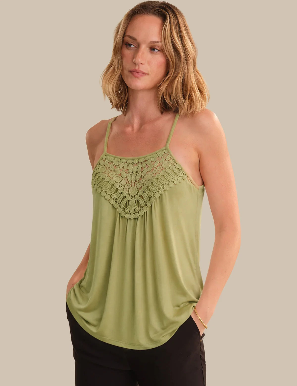 Woman wearing a green tank top with lace detailing on a beige background
