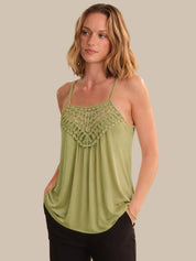 Woman wearing a green tank top with lace detailing on a beige background