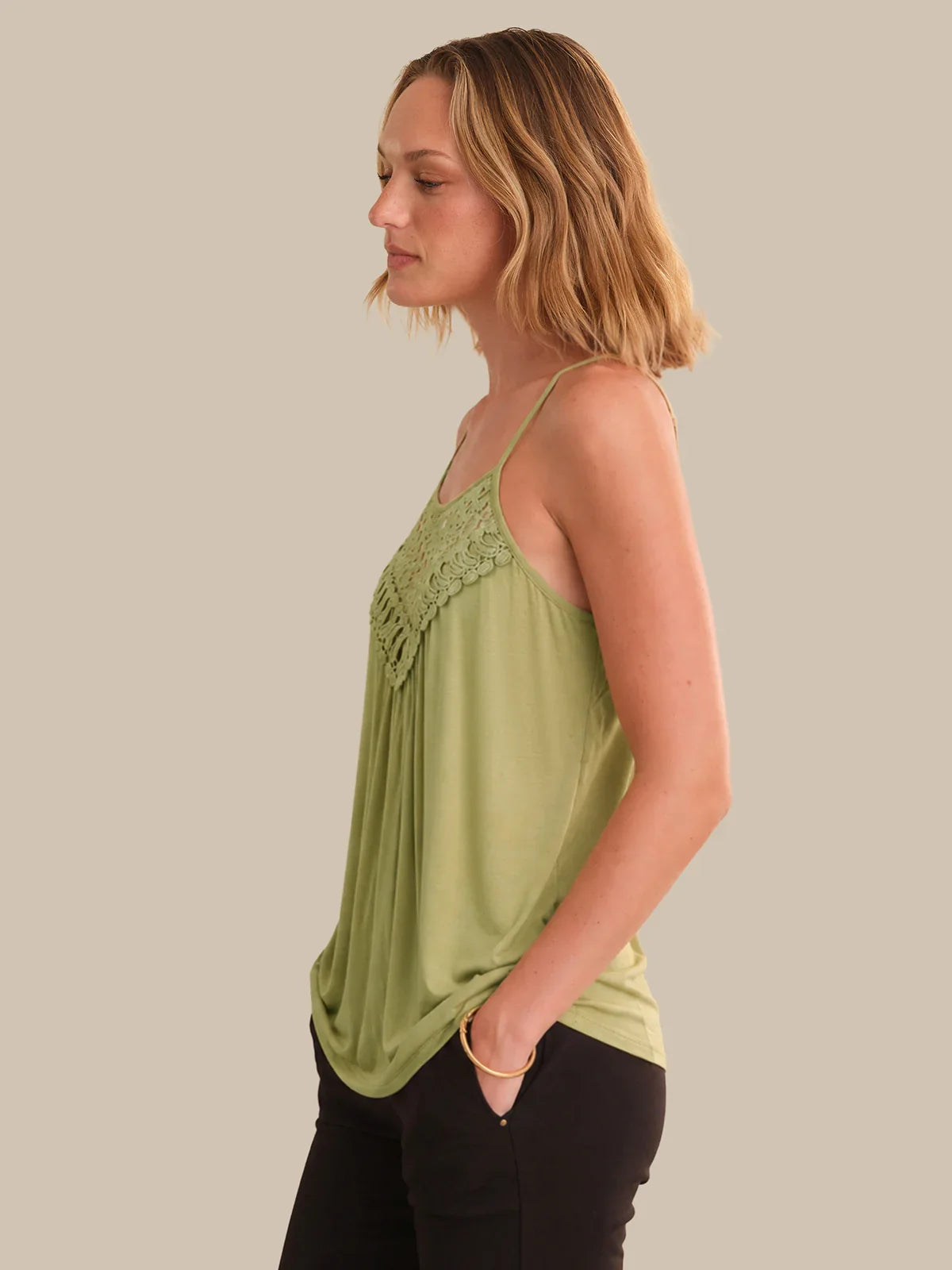 Woman wearing a green lace-trimmed top against a plain background