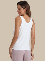 A woman shown from the back wearing a white sleeveless tank top and mauve pants, against a solid beige background.
