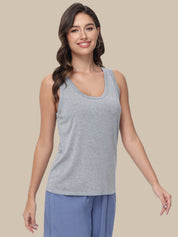 A woman modeling a light gray heather scoop-neck tank top paired with blue pants, set against a solid beige background.