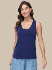 A woman modeling a solid navy blue scoop-neck tank top paired with light blue denim shorts, set against a solid beige studio background.