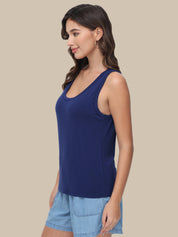 A woman wearing a navy blue scoop-neck tank top and light blue denim shorts, shown from a side profile against a solid beige background.