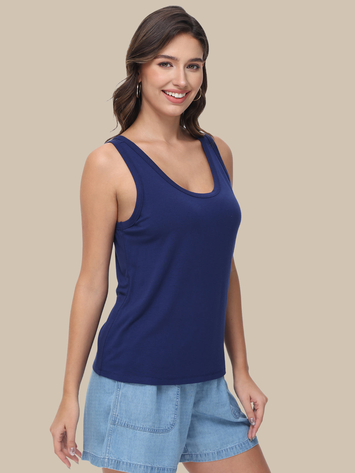 A woman modeling a navy blue scoop-neck tank top paired with light blue denim shorts, set against a solid beige background.