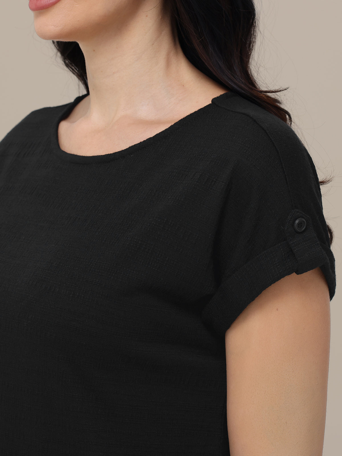 Close-up of a person wearing a black top with button details on a neutral background