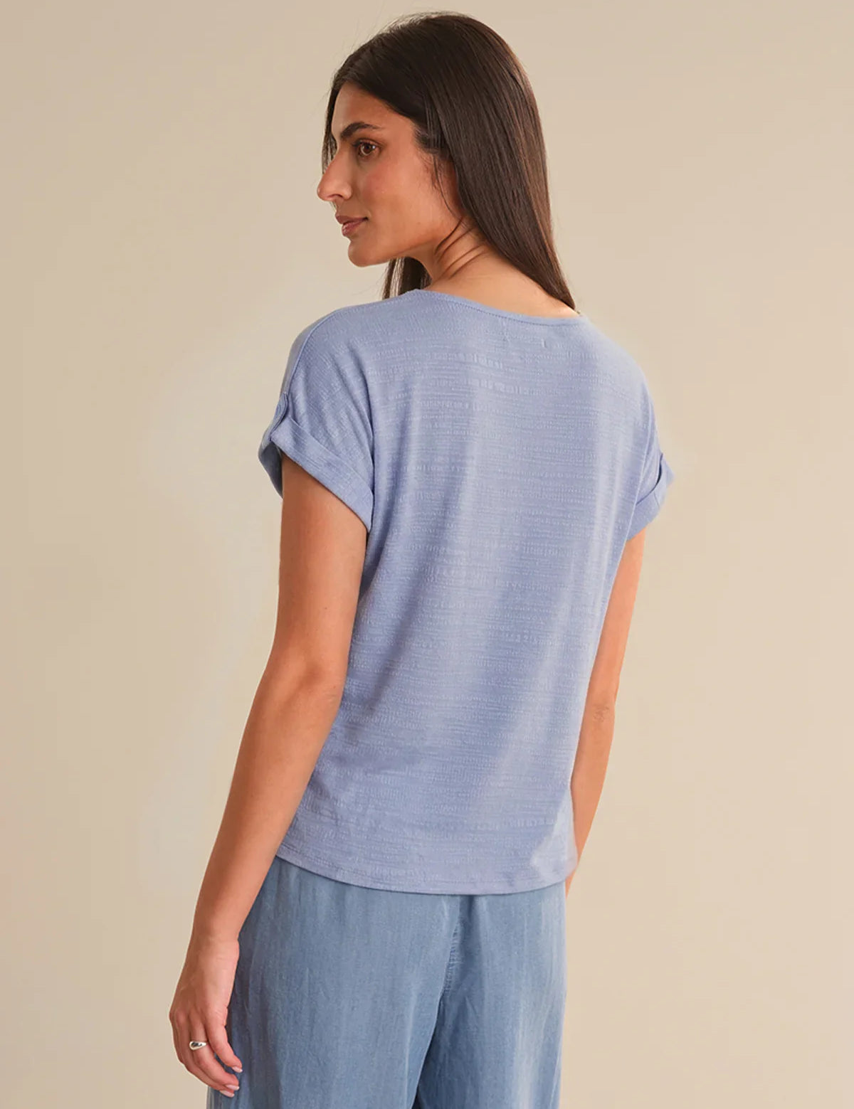Woman wearing a blue t-shirt and pants against a beige background
