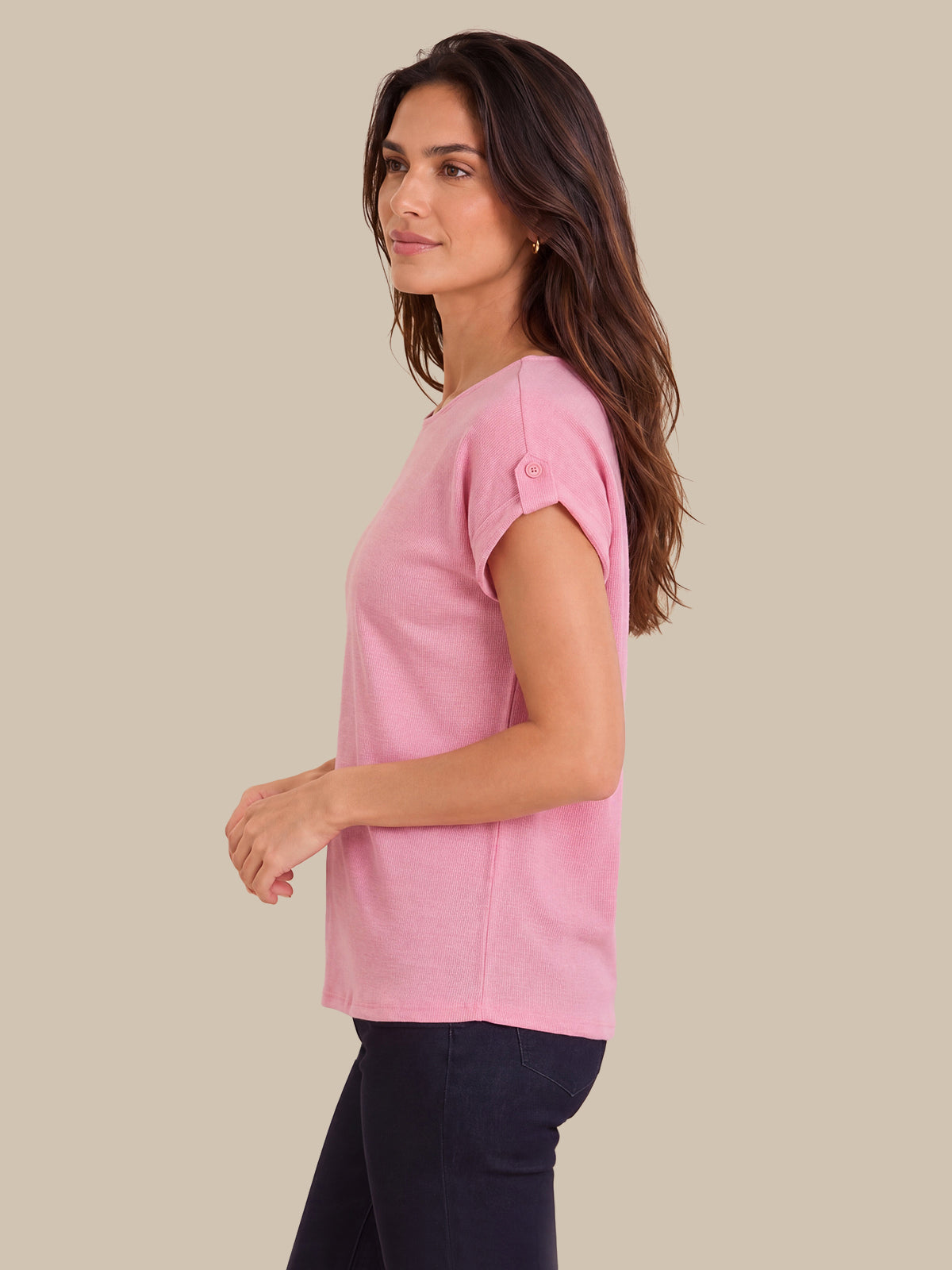 A woman wearing a light pink short-sleeve top with rolled cuffs and dark navy pants, shown in profile against a solid beige background.