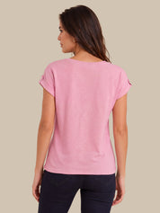 A woman shown from the back wearing a light pink short-sleeve t-shirt and dark navy pants, set against a solid beige background.