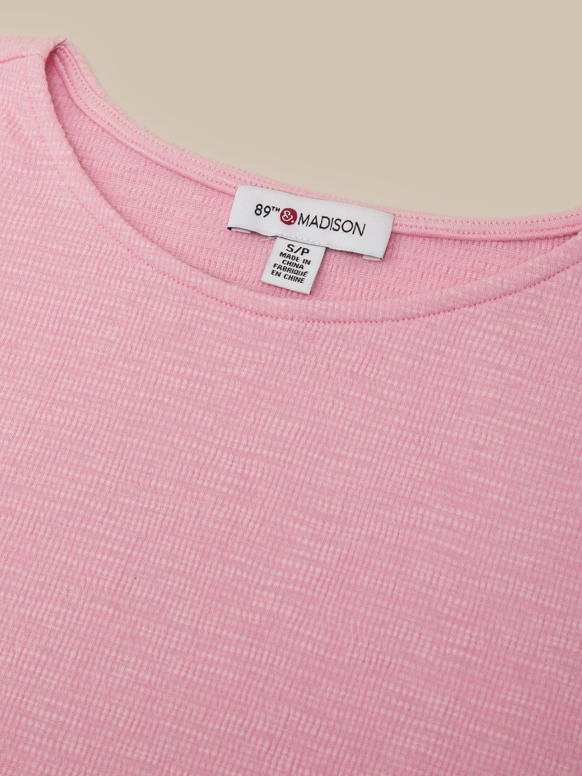 Close-up of a pink ribbed knit top showing the inside neckline with a white brand label that reads 89F MADISON.