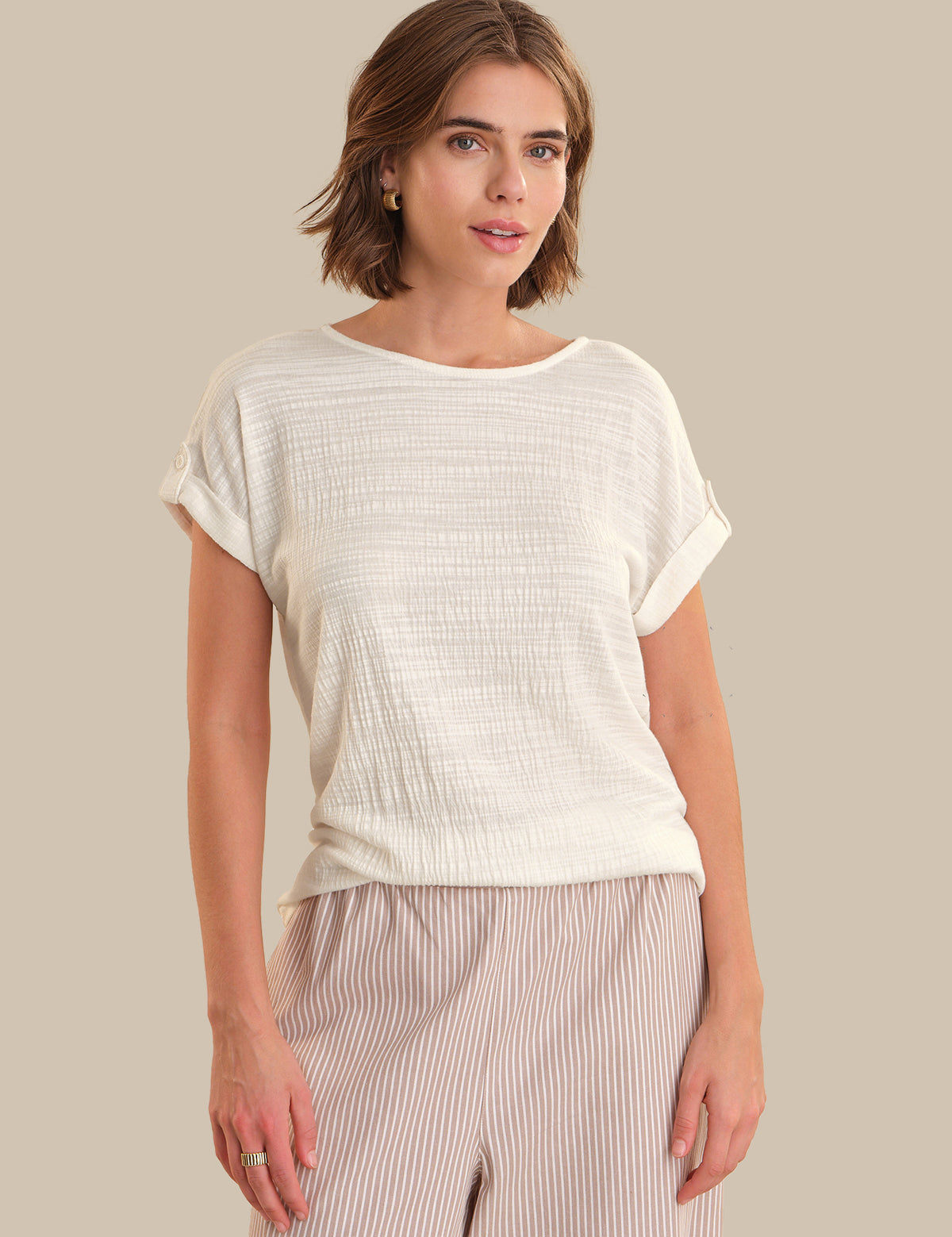 Woman wearing a white textured top and beige pants against a plain background