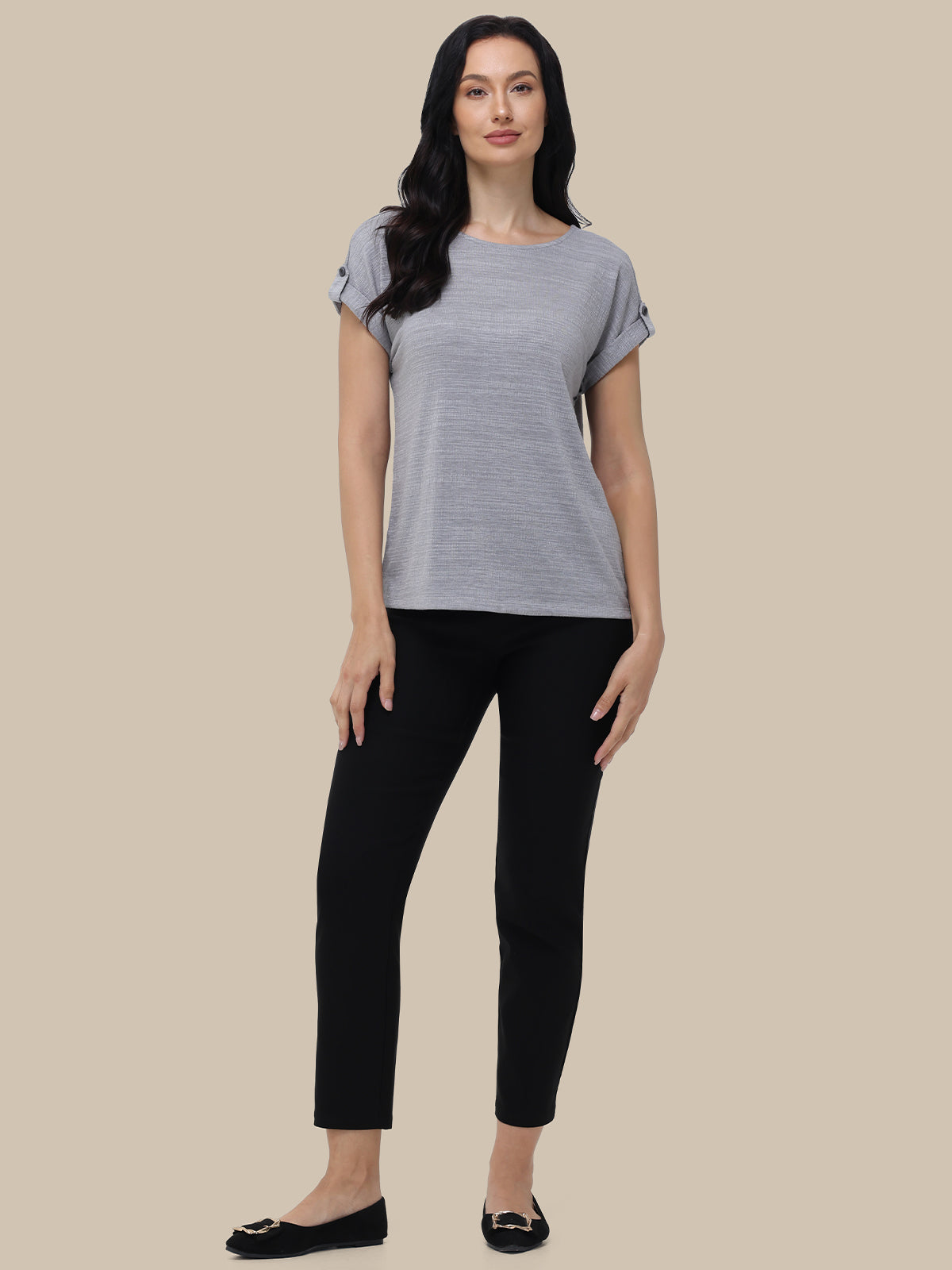 Woman wearing a gray striped shirt and black pants on a beige background