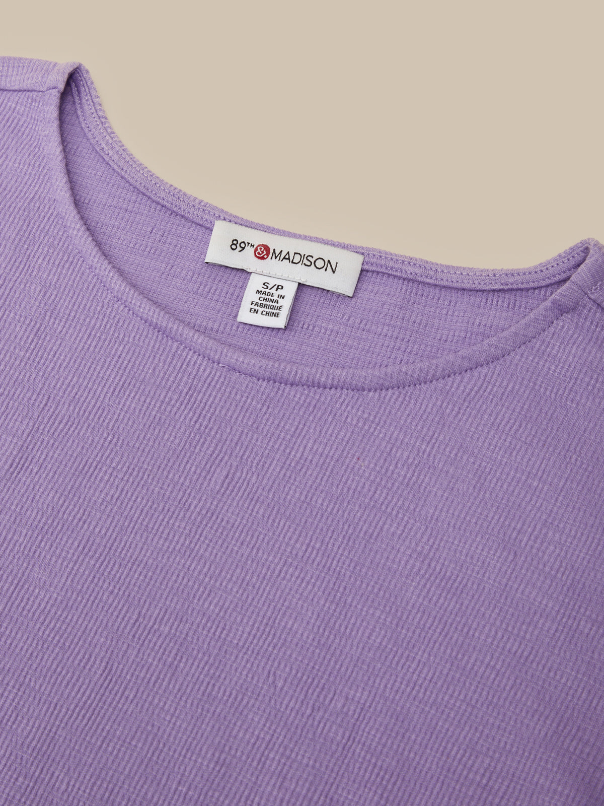 Close-up of a lavender ribbed knit top showing the inside neckline with a white tag that reads 89 Madison.
