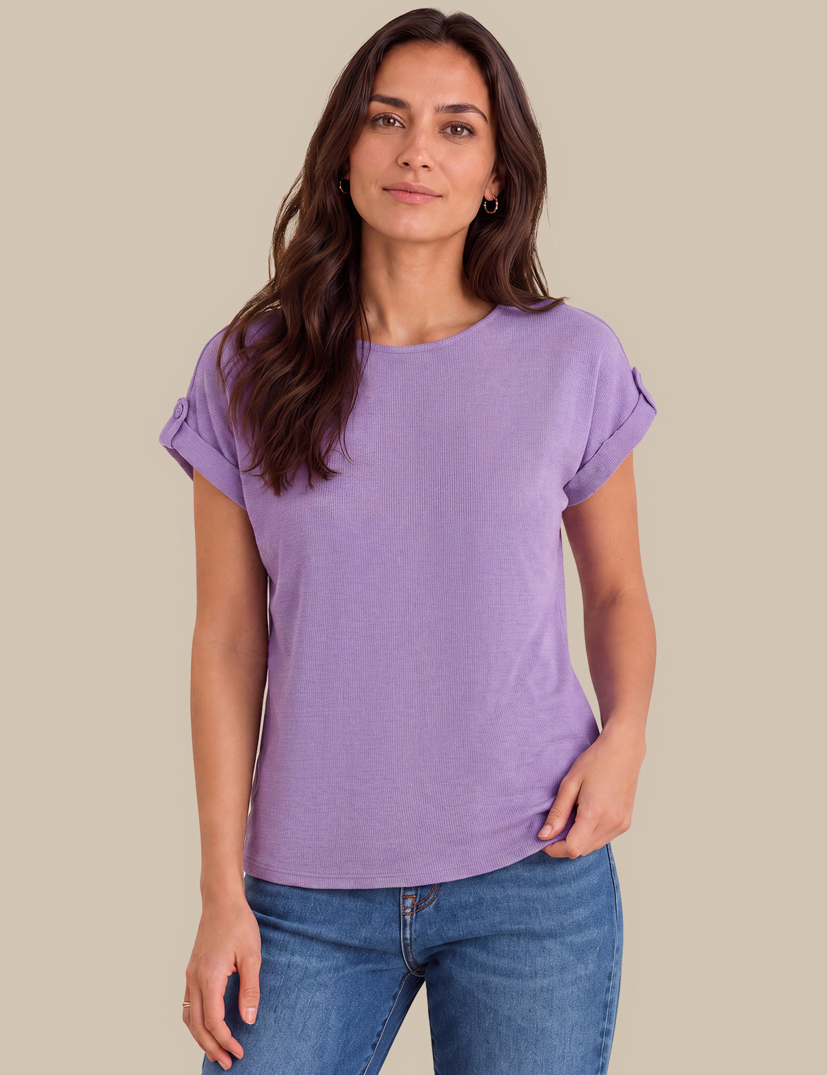 A woman modeling a lavender short-sleeve crewneck t-shirt with rolled cuffs, paired with blue jeans, against a solid beige background.