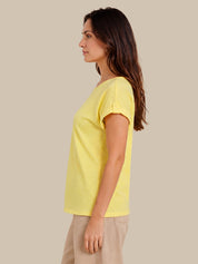 A woman shown in side profile wearing a short-sleeve yellow top and beige pants against a plain beige studio background.