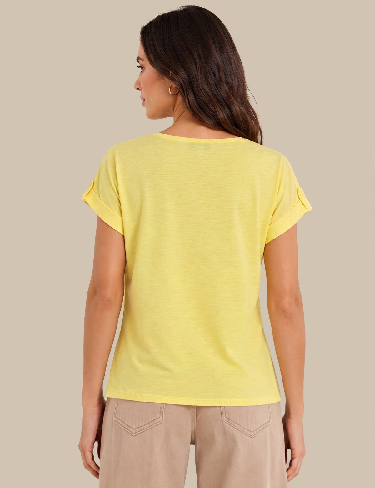 A woman shown from the back wearing a light yellow short-sleeve t-shirt with rolled cuffs and beige pants, set against a solid beige background.