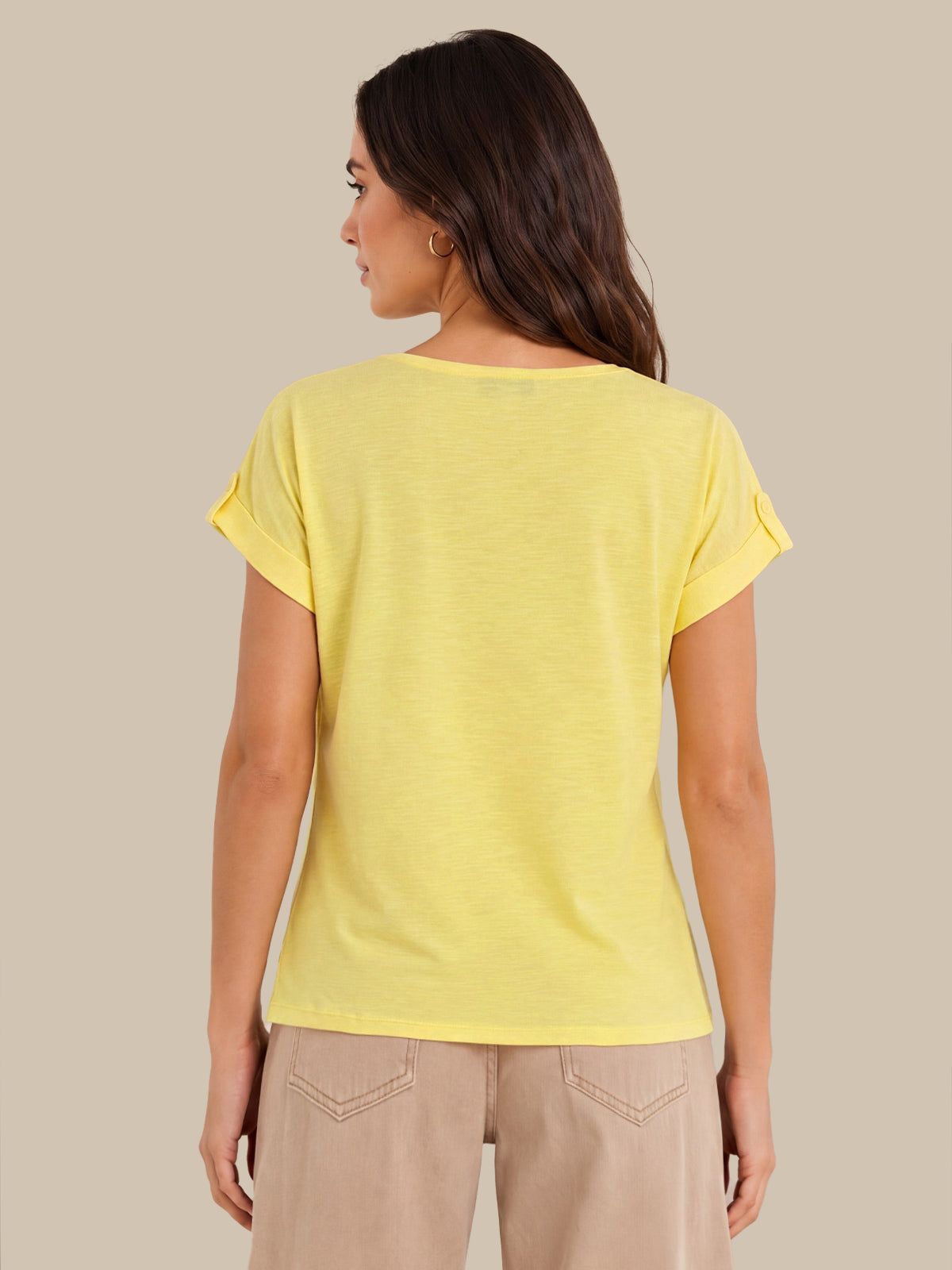 A woman shown from the back wearing a light yellow short-sleeve t-shirt with rolled cuffs and beige pants, set against a solid beige background.