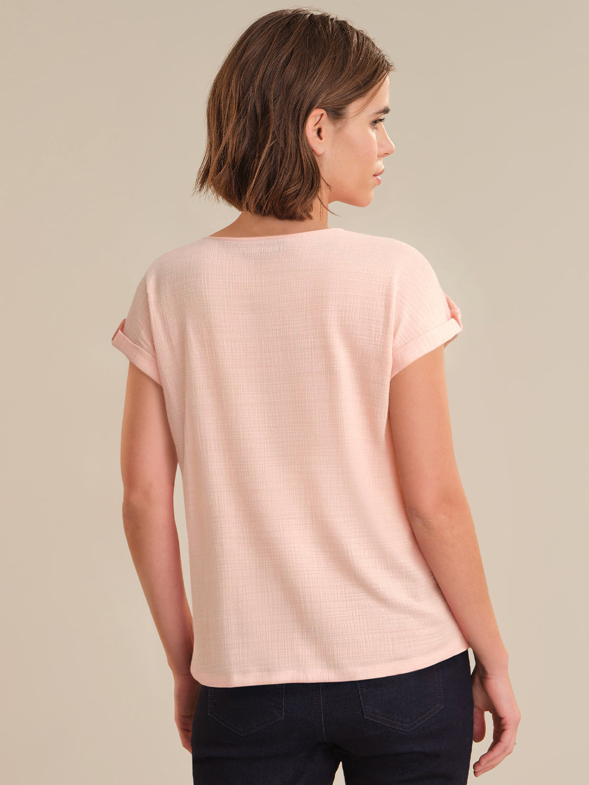 Woman wearing a light pink t-shirt against a beige background