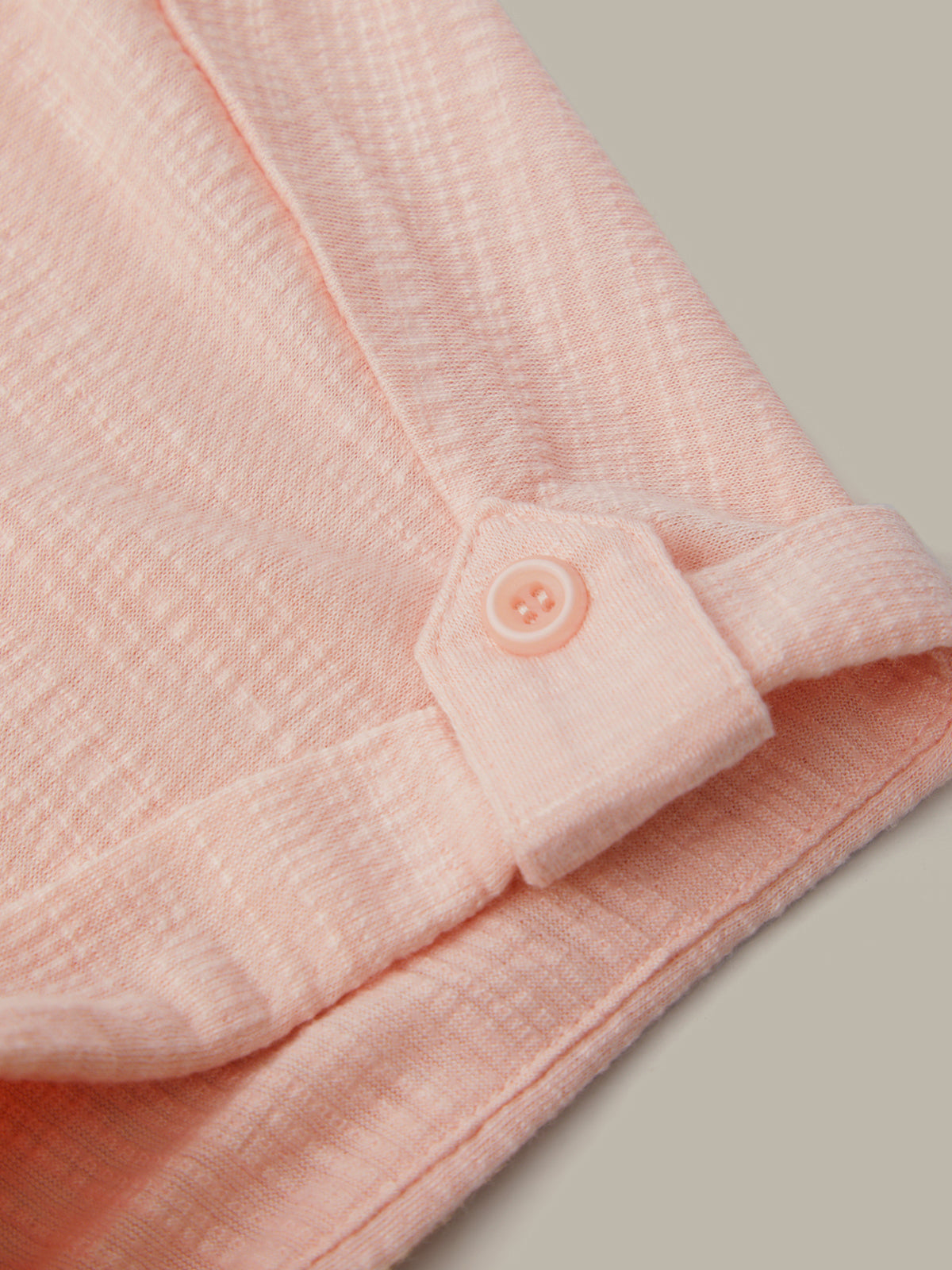 Close-up of a pink textured fabric with a button on a neutral background