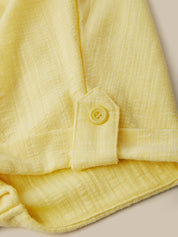 Close-up of a yellow textured fabric with a button on a neutral background