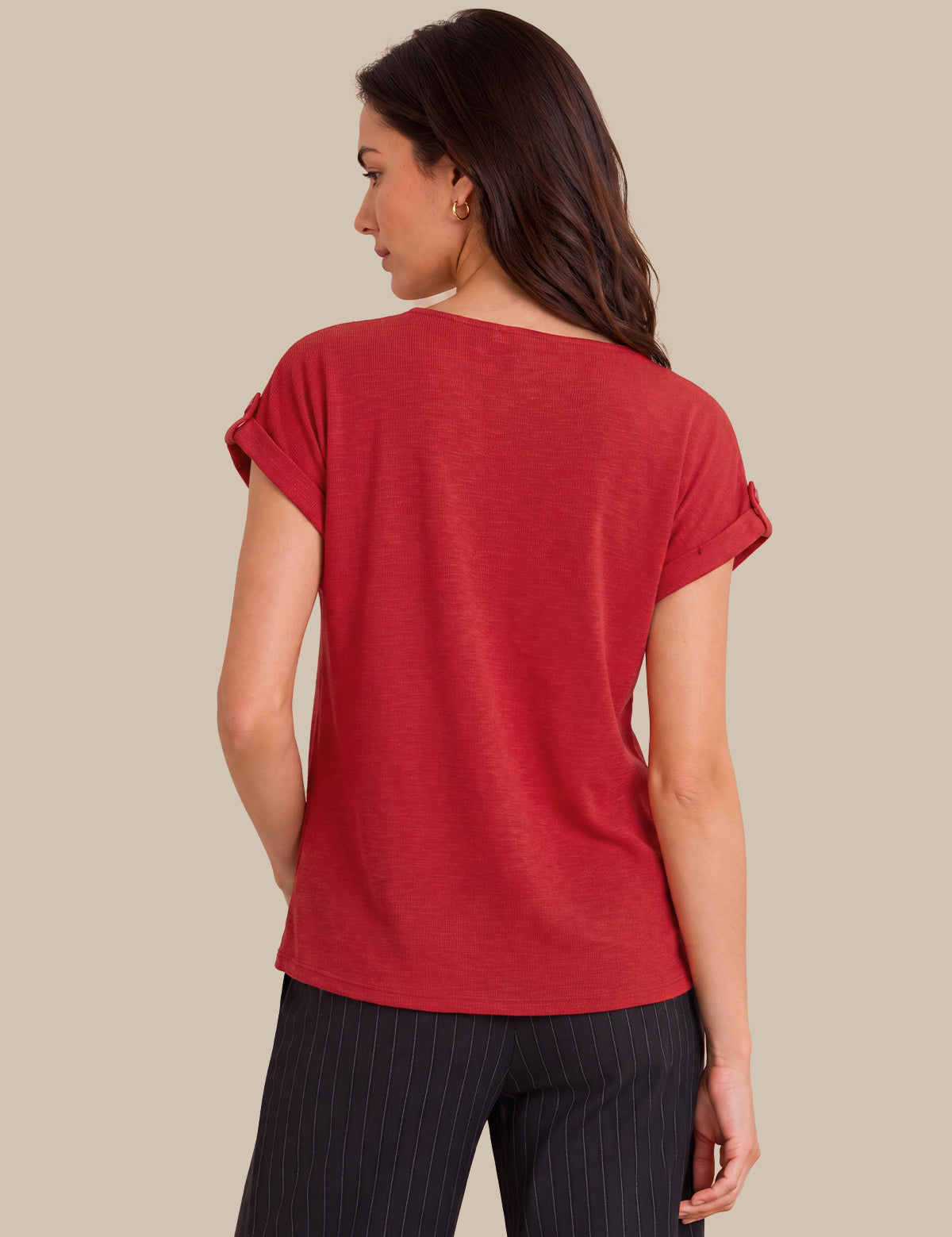 A woman shown from the back wearing a red short-sleeve top with rolled cuffs and dark pinstriped pants, against a solid beige background.