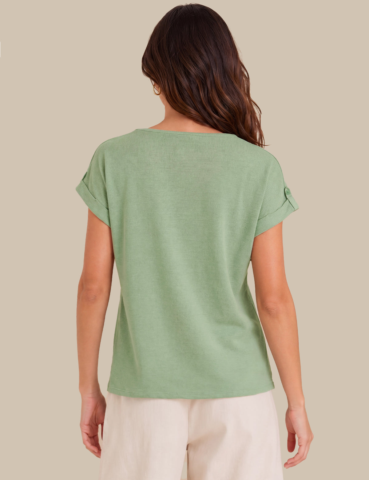 A woman viewed from the back wearing a light sage green short-sleeve top and cream pants, set against a solid beige background.