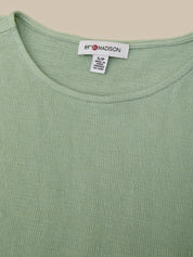 Close-up of a light sage green ribbed knit top with a white neck label reading 89° MADISON.