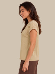 A woman shown in side profile wearing a light beige short-sleeve knit top and brown pants against a solid beige studio background.