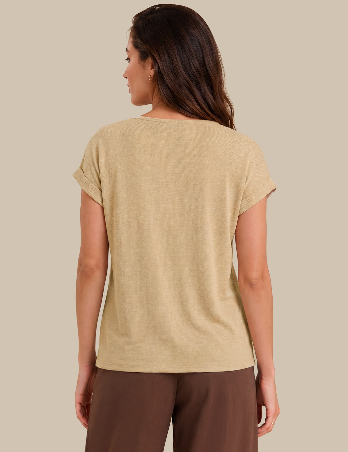 A woman shown from the back wearing a short-sleeve beige t-shirt and brown pants, photographed against a solid light beige background.