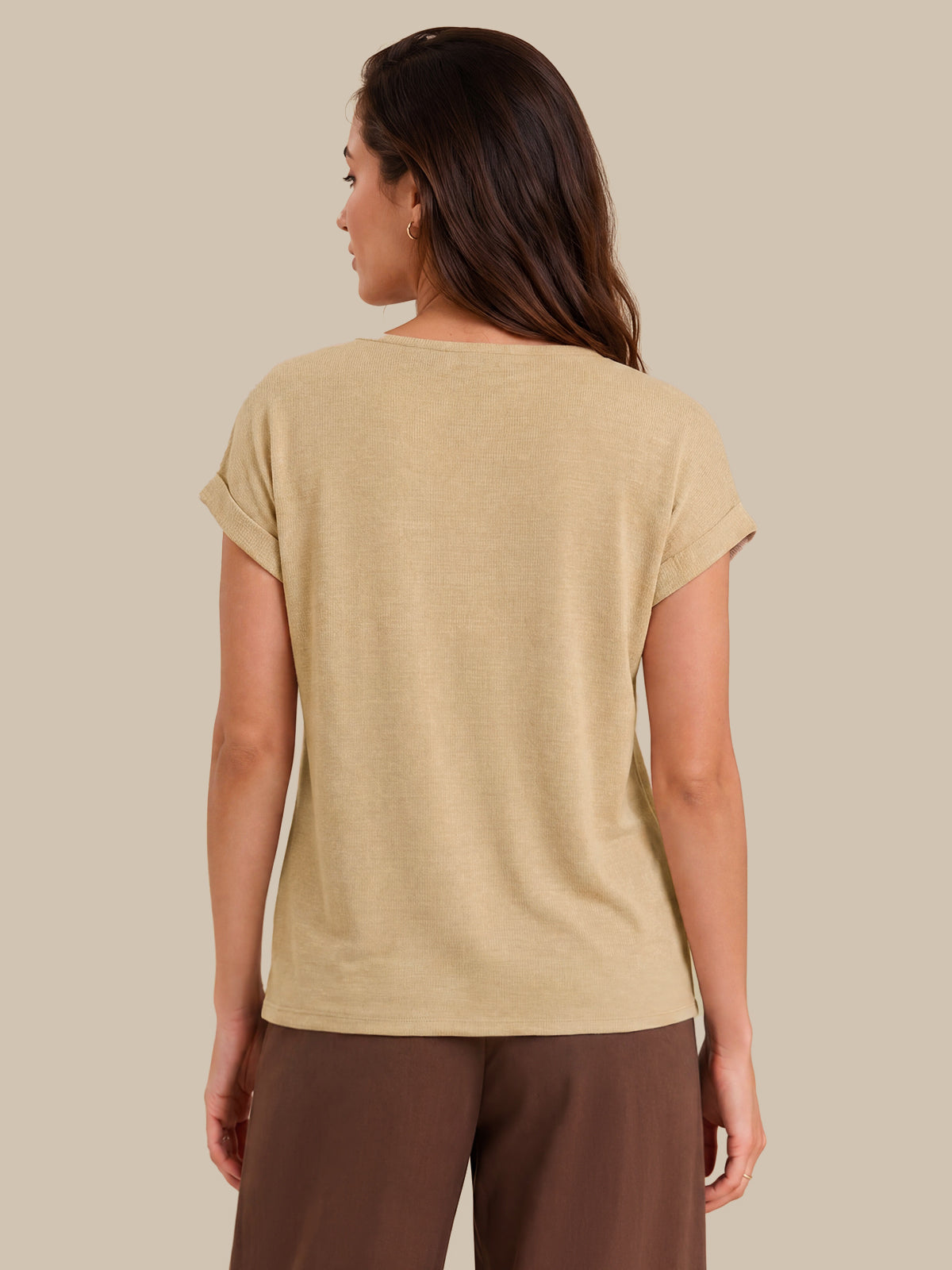A woman shown from the back wearing a short-sleeve beige t-shirt and brown pants, photographed against a solid light beige background.