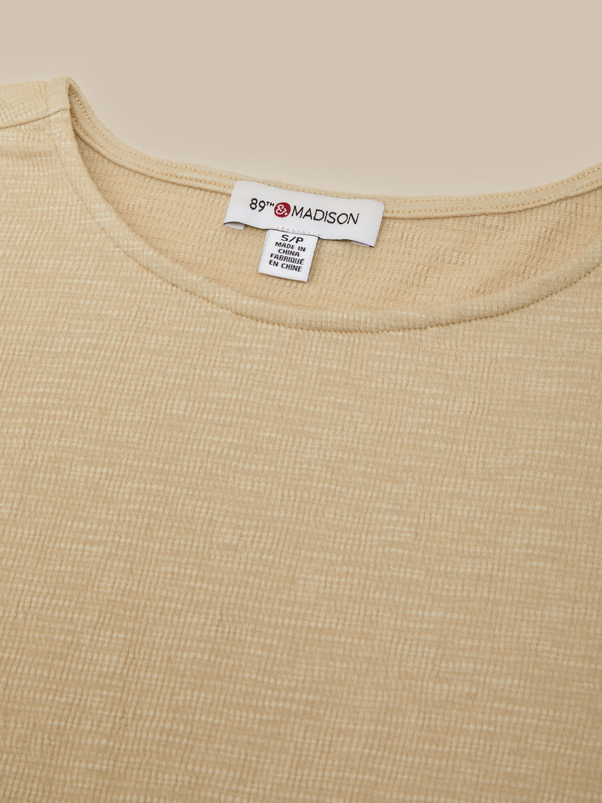 Close-up of a beige ribbed knit top showing the inner neck label which reads '89 MADISON'.
