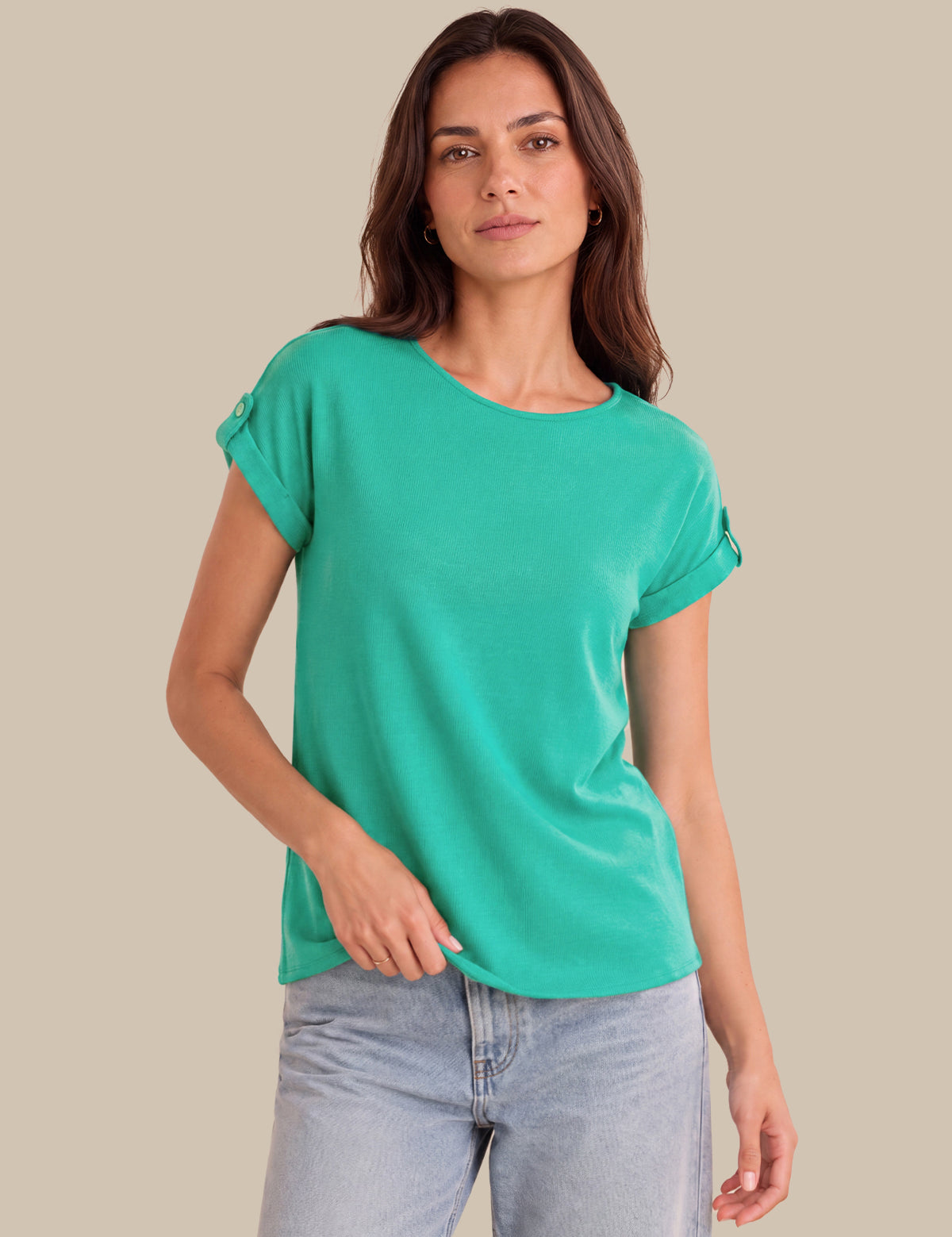 A woman wearing a short-sleeve crewneck t-shirt in a vibrant mint green color, paired with light-wash blue jeans, set against a solid beige studio background.