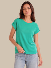 A woman wearing a short-sleeve crewneck t-shirt in a vibrant mint green color, paired with light-wash blue jeans, set against a solid beige studio background.