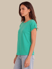 A woman wearing a bright green short-sleeve t-shirt with rolled cuffs and light blue jeans, shown from a side profile against a solid beige background.