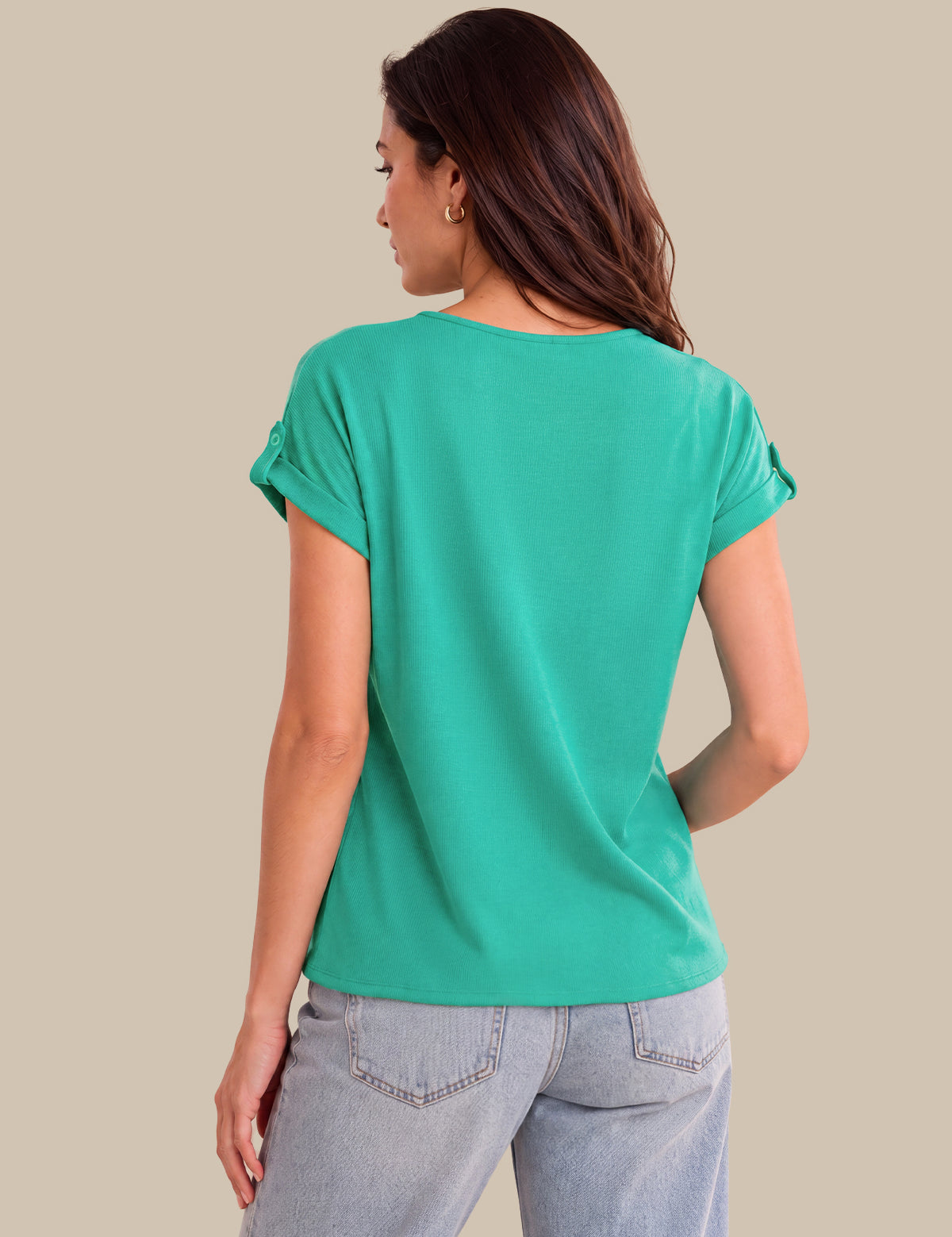 A woman shown from the back wearing a short-sleeve teal green top and light-wash jeans, photographed against a plain beige studio background.