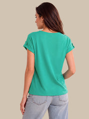 A woman shown from the back wearing a short-sleeve teal green top and light-wash jeans, photographed against a plain beige studio background.