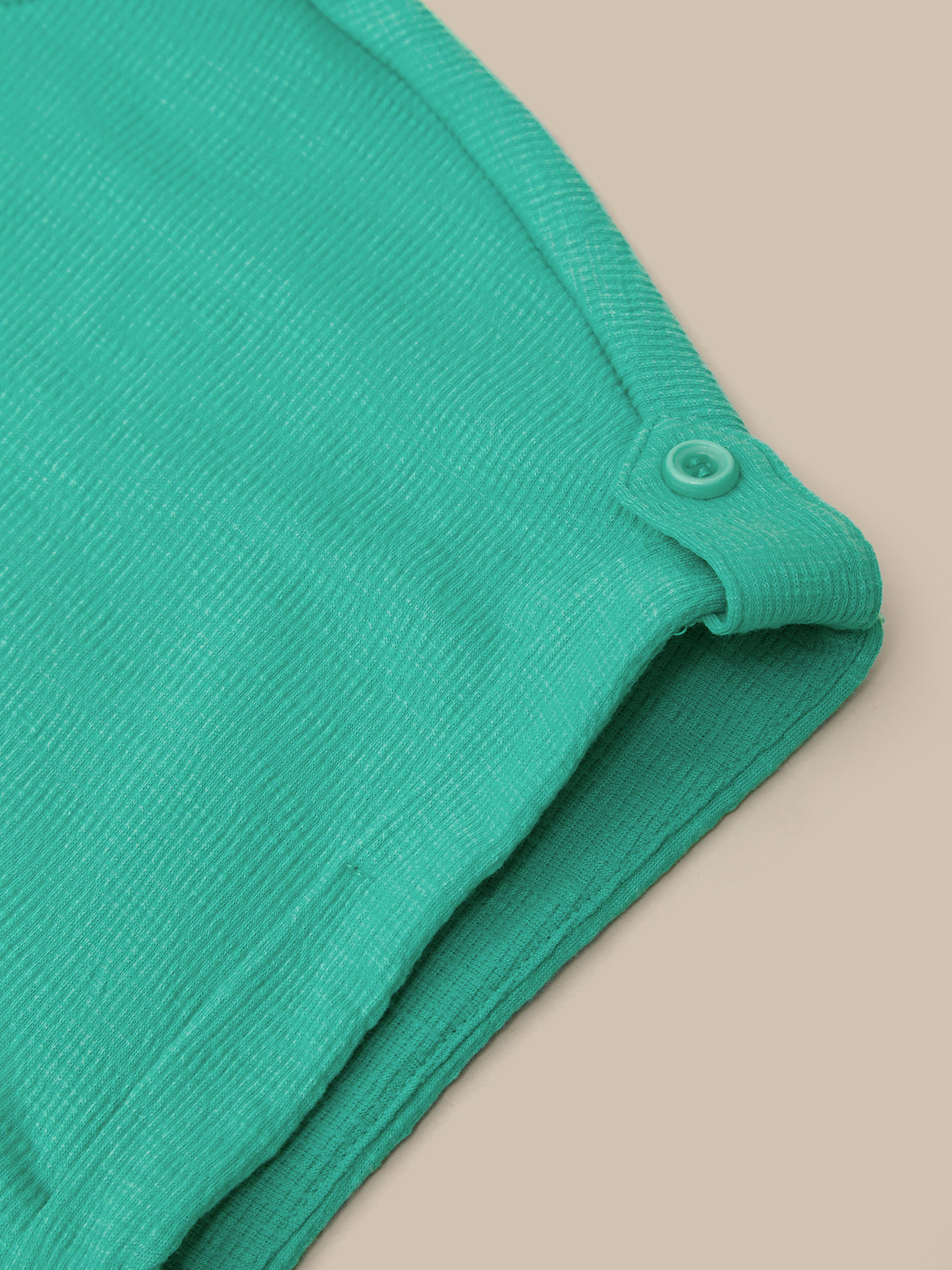Close-up of a folded mint green ribbed knit garment, showing a buttoned neckline detail against a solid beige background.