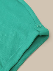 Close-up of a folded mint green ribbed knit garment, showing a buttoned neckline detail against a solid beige background.