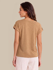 A woman shown from the back wearing a tan short-sleeve top with rolled cuffs and light-colored pants, set against a solid beige background.