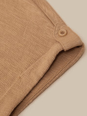 Close-up of a folded tan ribbed fabric item with a small matching button detail, shown on a plain warm beige background.