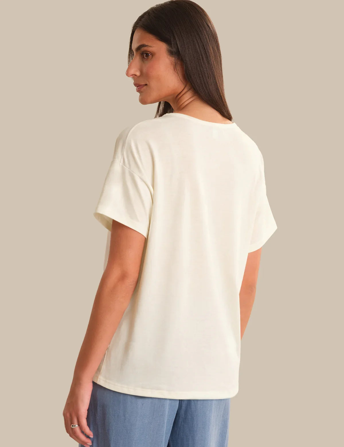 Woman wearing a white t-shirt and blue pants on a beige background