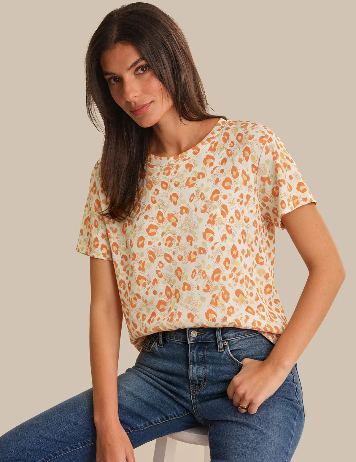 Woman wearing a leopard print top and blue jeans on a beige background