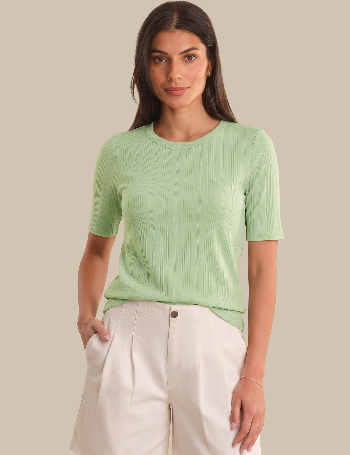Woman wearing a light green ribbed t-shirt and white pants against a beige background