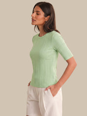 Woman wearing a light green ribbed sweater against a beige background