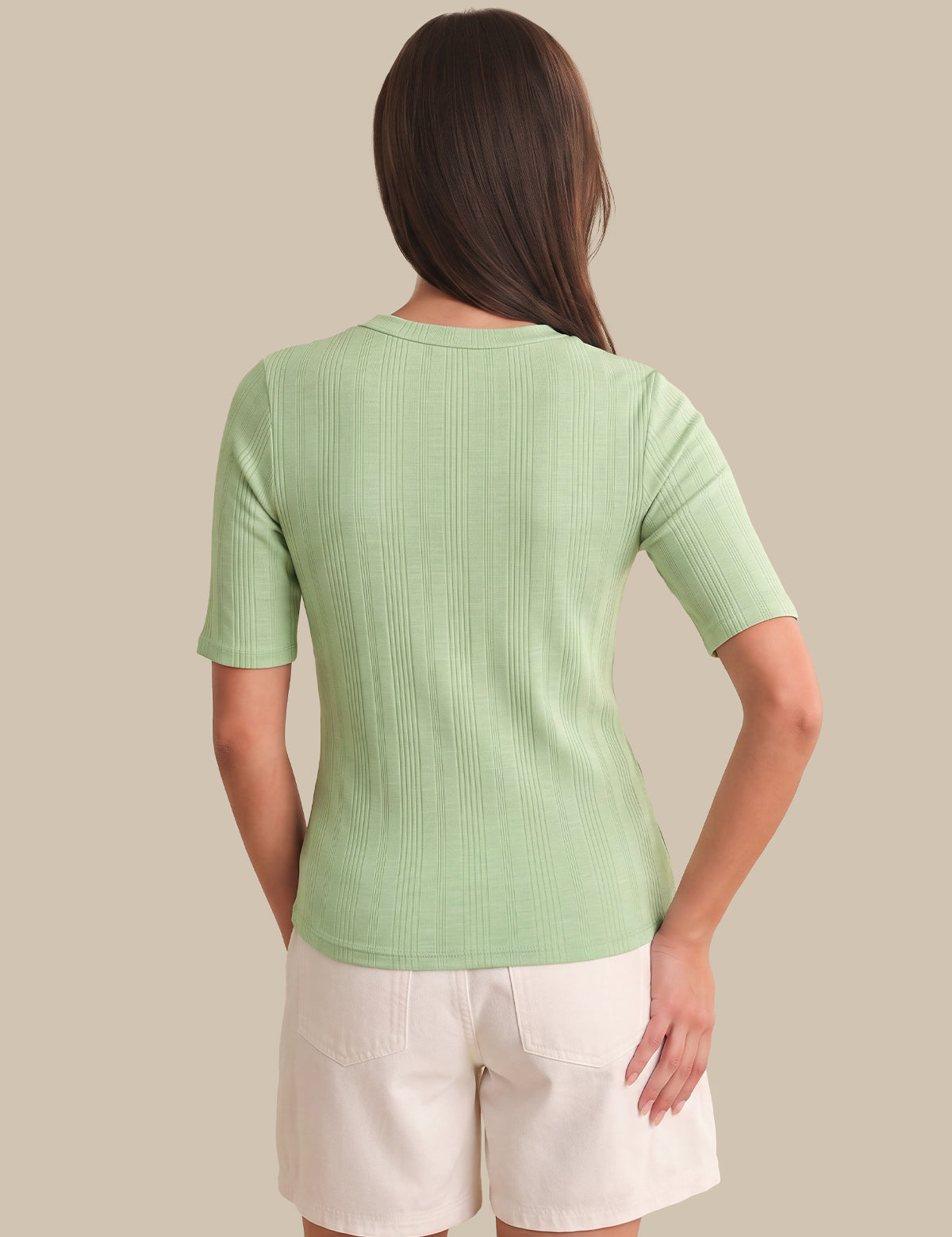 Woman wearing a green ribbed sweater and white shorts on a beige background