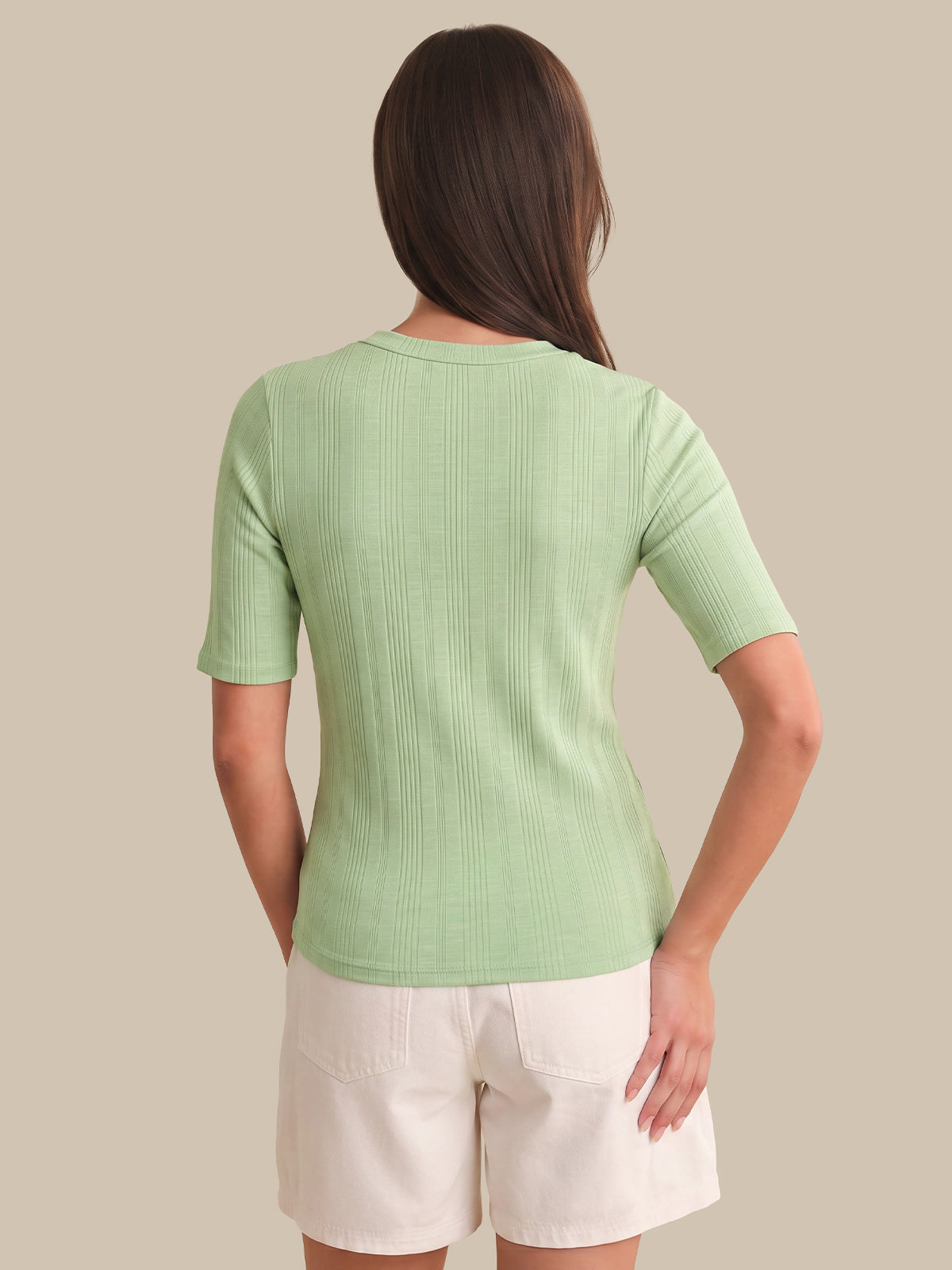Woman wearing a green ribbed sweater and white shorts on a beige background